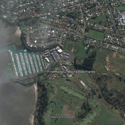 Google Earth aerial view of Pine Harbour Marina and Beachlands, New Zealand, showing rows of boats docked in the marina along the coastline, surrounded by residential neighborhoods, roads, green space, and a golf course.