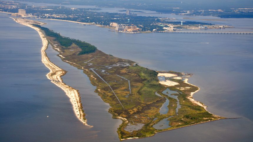 Aerial view of Deer Island showing marsh habitat, tidal channels, sandy shoreline, and surrounding coastal waters, with developed shoreline in the distance.