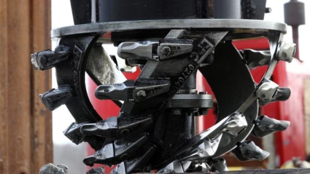 Close-up of a heavy-duty rotary cutting or dredging head fitted with multiple metal teeth, used to excavate or break up sediment during marsh restoration work.